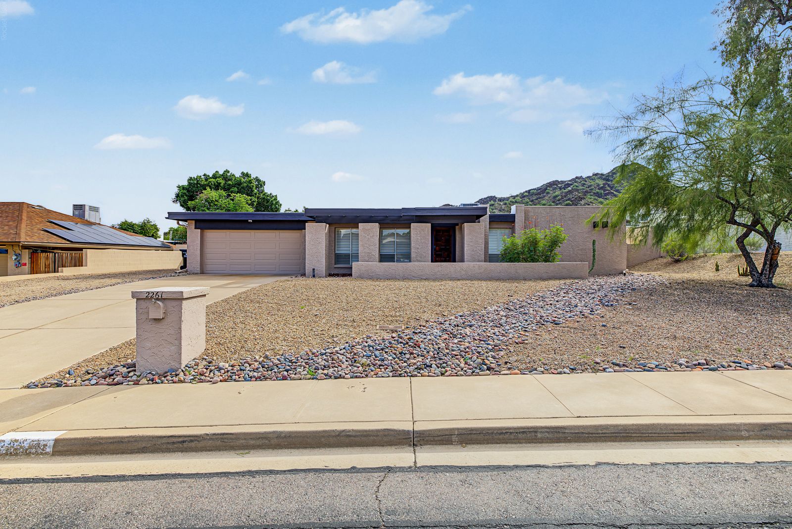 Front of the single-level home with a two-car garage and desert landscaping, mountain behind